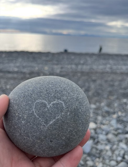 Gray beach rock with a hand-drawn heart held by the water